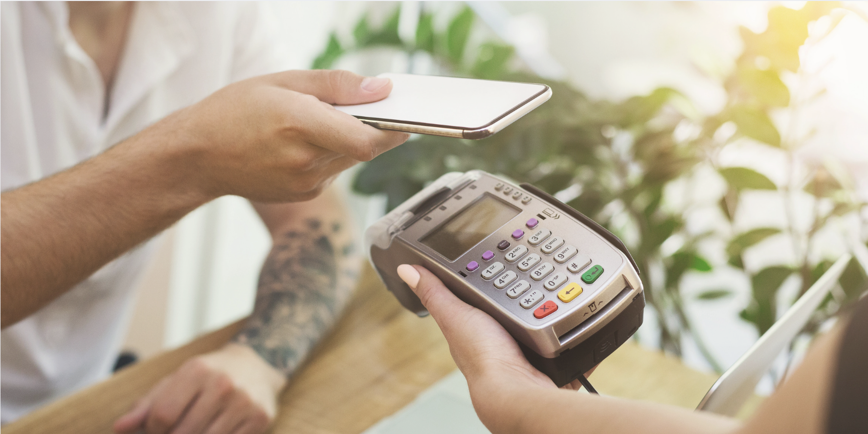 Client effectuant un paiement sans contact avec un téléphone intelligent à l’aide d’un terminal de paiement portable dans un café.