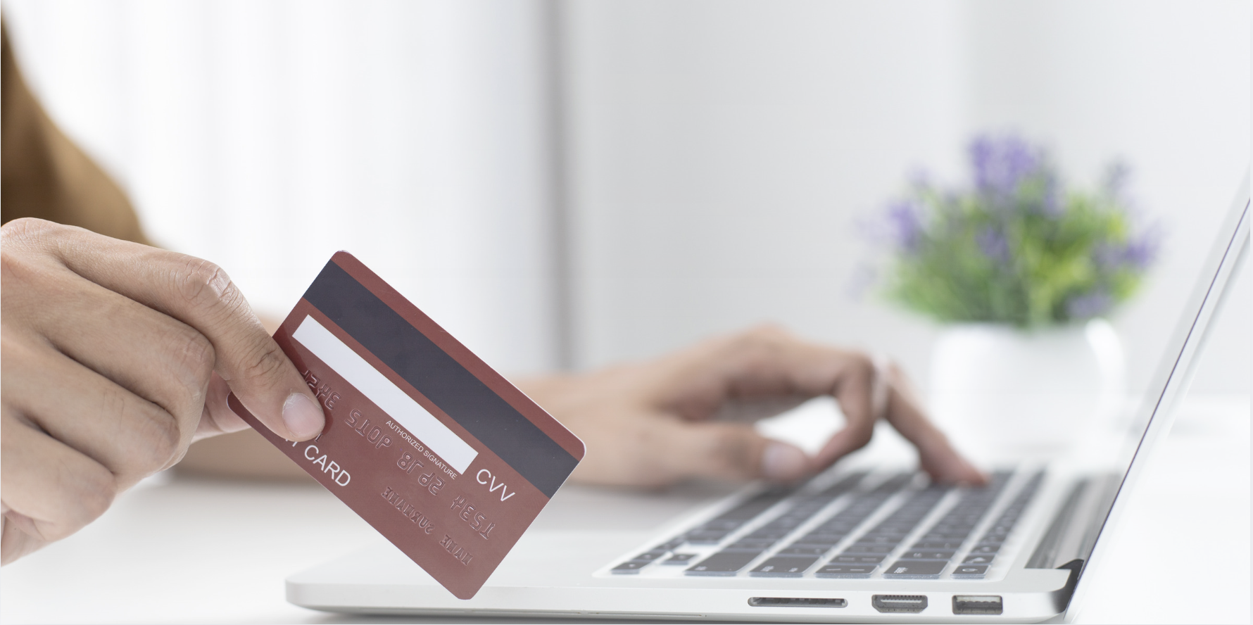 Person holding a credit card while using a laptop to complete an online purchase, with the card in focus and the computer keyboard blurred in the background.